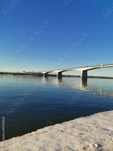 Bridge over the Kama River, early spring, reflection of the blue sky in the water. © Bella