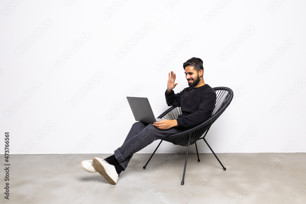 Young man freelancer is at home, sits in a chair and communicates online. A young man on a laptop eran uses a video call and video chat. Working online, remote communication.
