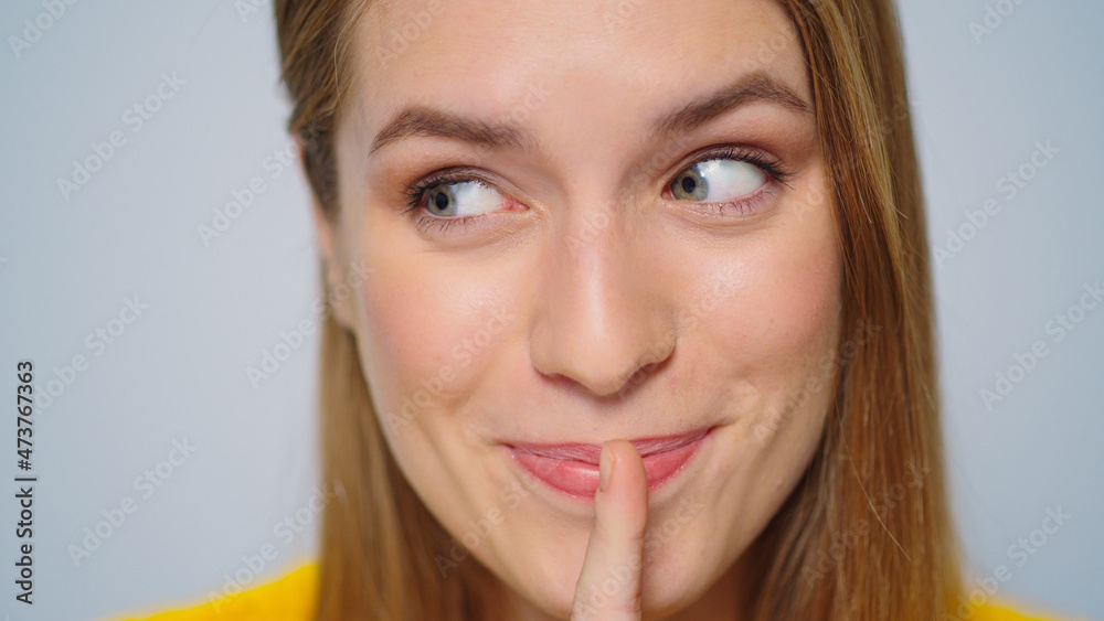Closeup cheerful woman showing silence sign in studio camera on grey background. Closeup cheerful woman showing silence sign in studio camera on grey background.