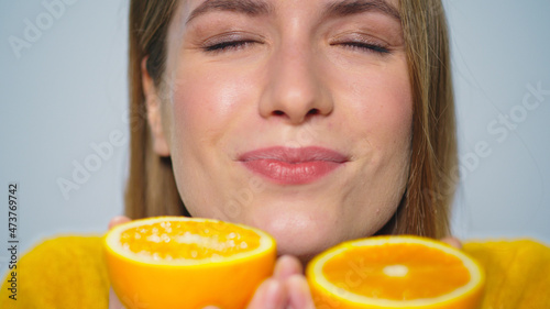 Closeup cheerful woman having fun with two orange slices at camera in studio. 