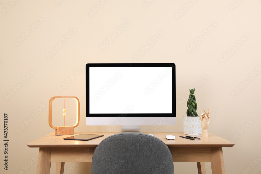 Comfortable workplace with blank computer display on desk and plant near beige wall. Space for text Comfortable workplace with blank computer display on desk and plant near beige wall. Space for text