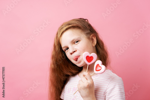 Tableau sur toile Girl holding big heart-shaped lollipops in her hands on a pink background