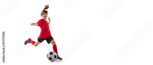Full-length portrait of sportive child, girl in red uniform playing, training football isolated over white background. Flyer