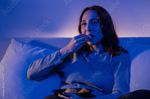 redhead young woman eating fruit while watching tv, woman having snack while watching tv at home