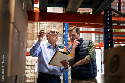 Two caucasian men in mature age discussing over documents together in warehouse