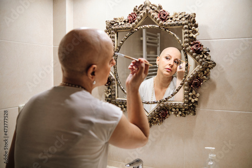 Mature woman with cancer brushing eyebrow while looking at reflection in mirror photo