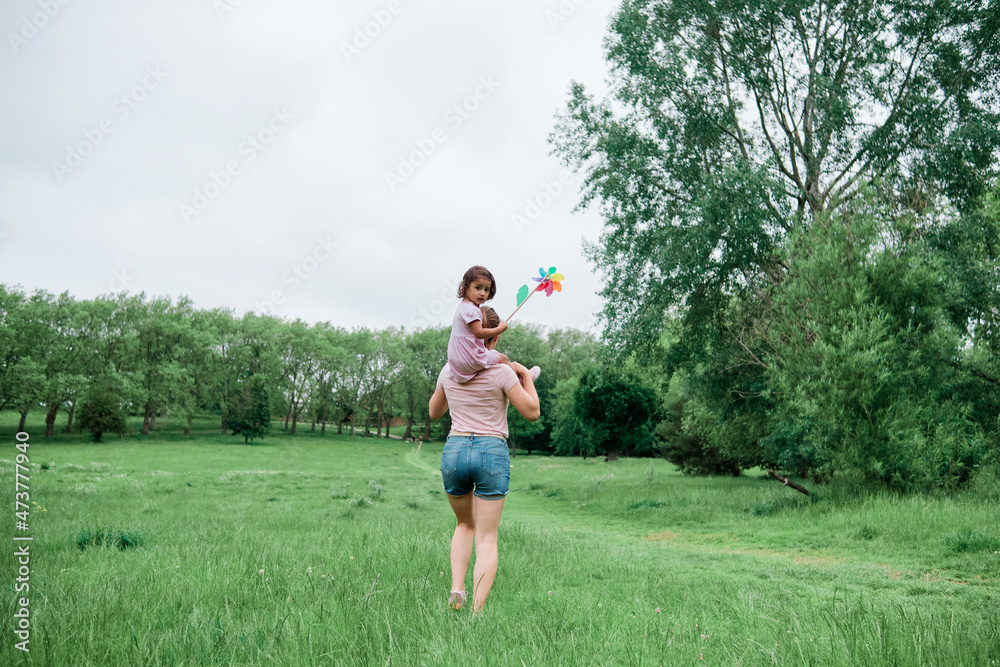 Mother carrying daughter on shoulders while walking in park Mother carrying daughter on shoulders while walking in park