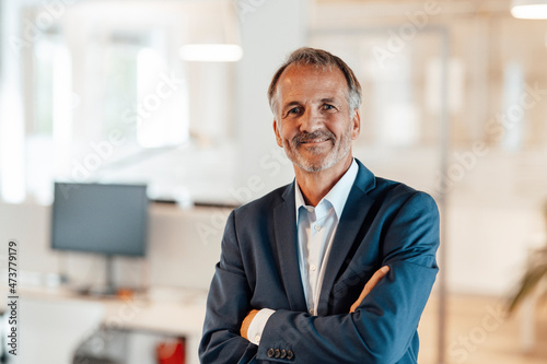 Male professional smiling while standing with arms crossed in office