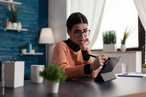 Student holding stylus browsing on digital tablet. Freelancer interacting with tablet-pc display using touch pen. Programmer with glasses in home studio casually using touchscreen device.