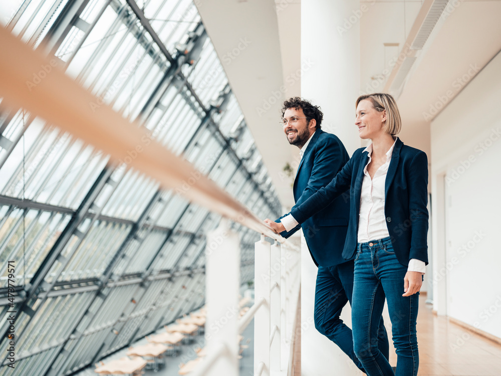 Smiling male and female entrepreneurs looking away while leaning on railing Smiling male and female entrepreneurs looking away while leaning on railing