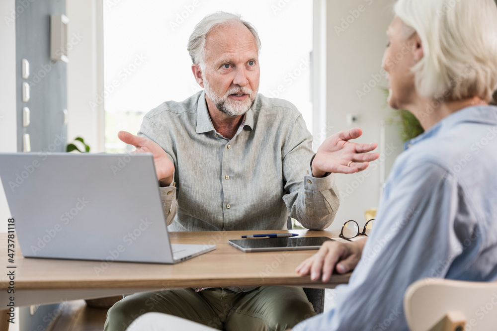 Male professional discussing with female colleague at desk in home office Male professional discussing with female colleague at desk in home office