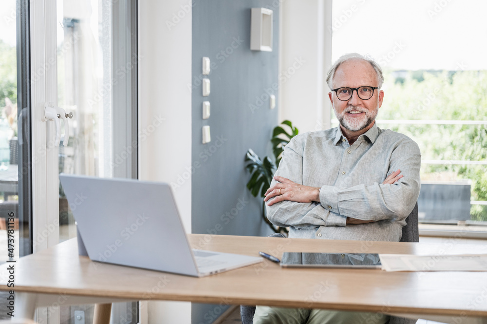 Businessman with arms crossed sitting at desk in home office Businessman with arms crossed sitting at desk in home office