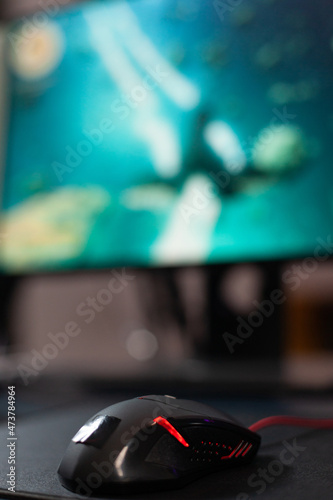 Close up of mouse in front of computer on desk. Mousepad and gaming equipment used to play video games online on monitor. Game on digital cyberpace with modern gadgets on table.