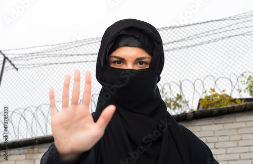 migration crisis, freedom and security concept - woman in hijab showing stop sign over barbed wire fence background photo