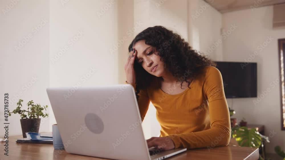 Concerned Multi-cultural female typing on laptop. Young professional remote working with laptop in modern apartment Concerned Multi-cultural female typing on laptop. Young professional remote working with laptop in modern apartment