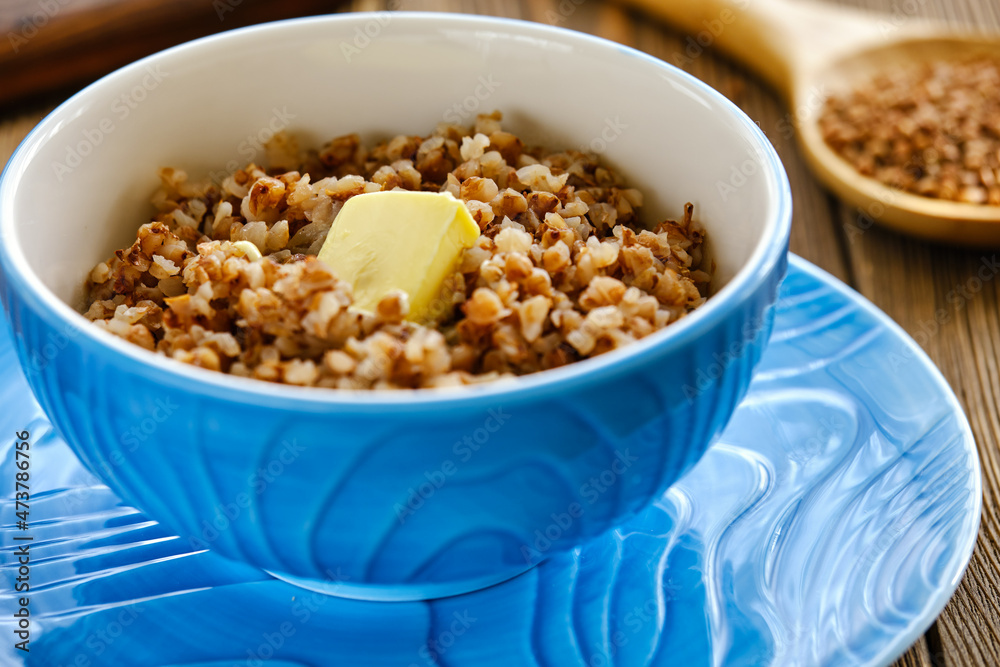 Fresh and tasty buckwheat porridge with butter in a blue cup on a wooden table Fresh and tasty buckwheat porridge with butter in a blue cup on a wooden table