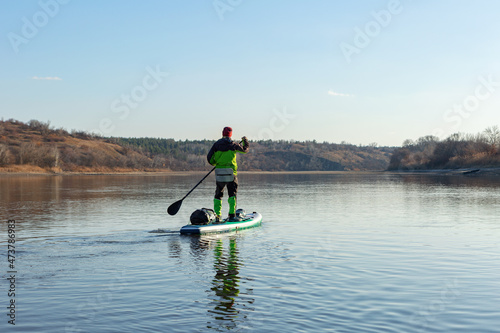 Late autumn on a clear day a man is rafting on a supboard on the river. SUP