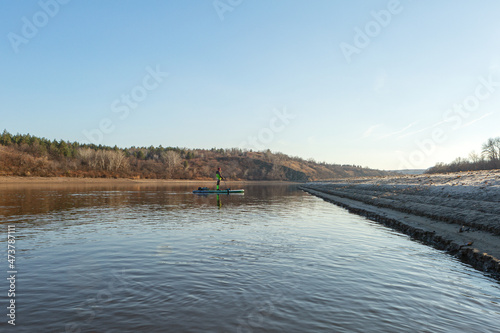 Late autumn on a clear day a man is rafting on a supboard on the river. SUP