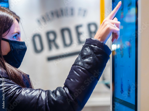Fényképezés Moscow, Russia -April 3, 2021: Pretty caucasian girl in a mask buys a hot drink at McDonald's