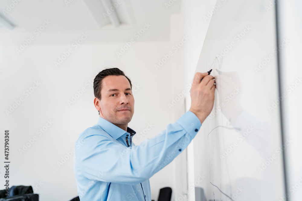 Male professional drawing chart on whiteboard at office Male professional drawing chart on whiteboard at office