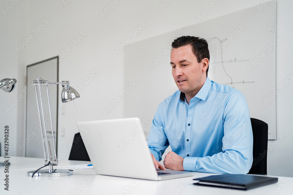 Male professional working on laptop at desk in office Male professional working on laptop at desk in office