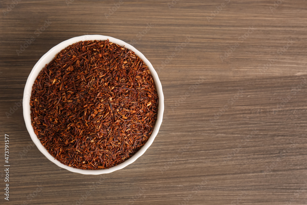 Dry rooibos leaves in bowl on wooden table, top view. Space for text Dry rooibos leaves in bowl on wooden table, top view. Space for text