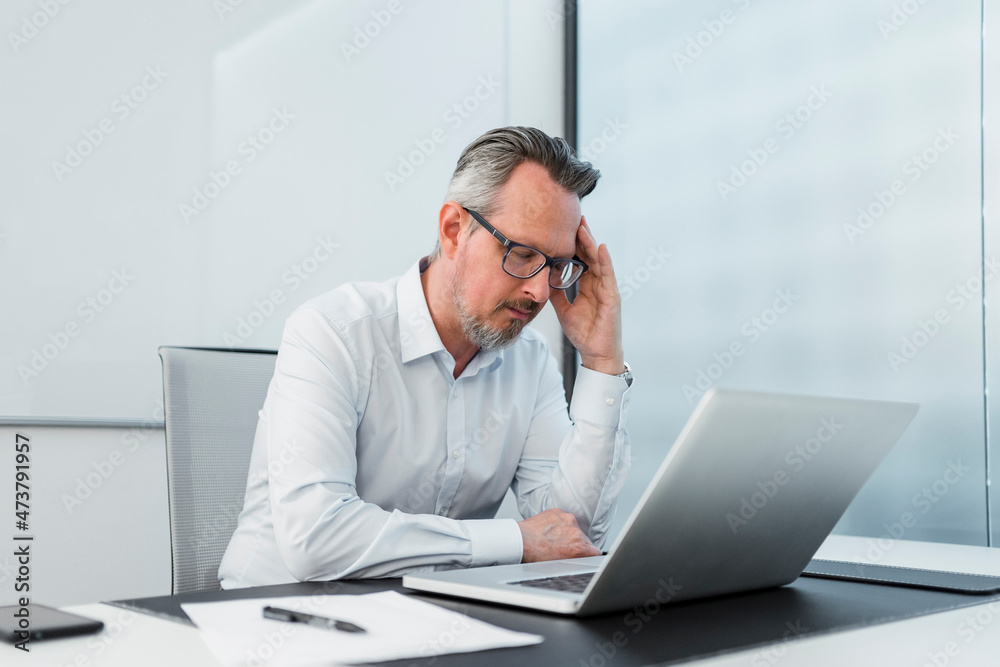 Businessman with head in hand sitting with laptop at desk Businessman with head in hand sitting with laptop at desk