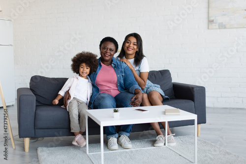joyful african american girl with mother and granny looking at camera while sitting on couch © LIGHTFIELD STUDIOS