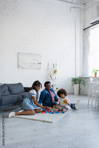 toddler african american child playing with colorful building blocks near granny and mom on floor in living room