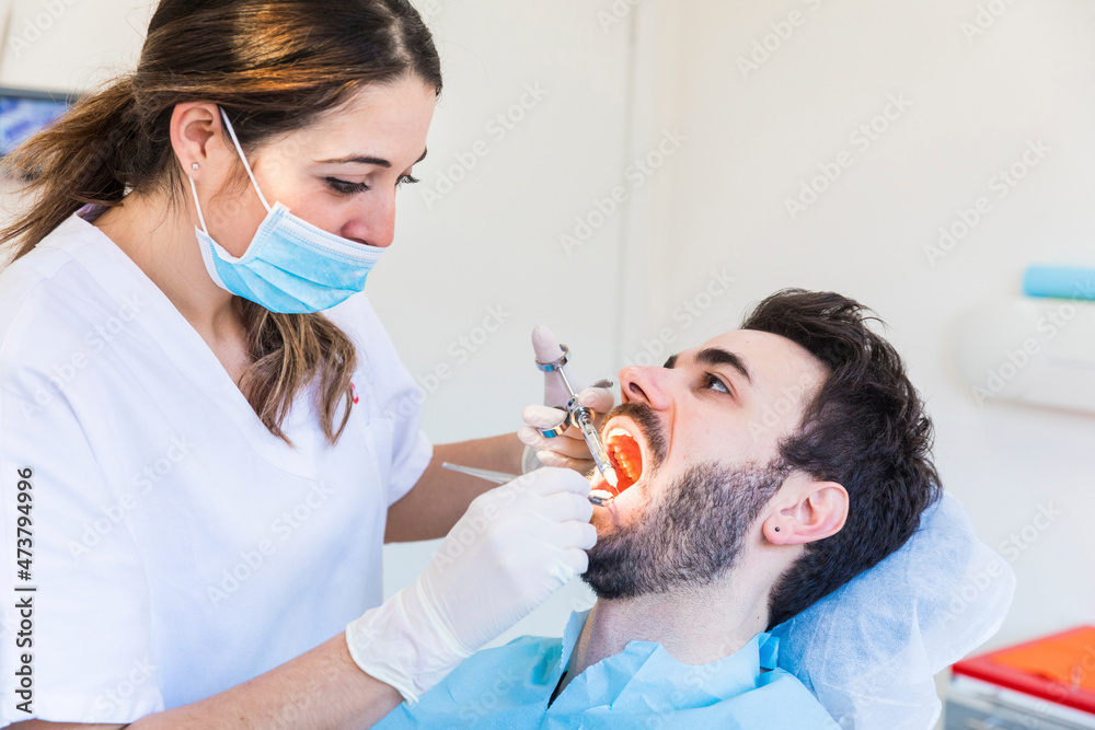 Female dentist wearing protective face mask examining male patient's teeth at medical clinic Female dentist wearing protective face mask examining male patient's teeth at medical clinic