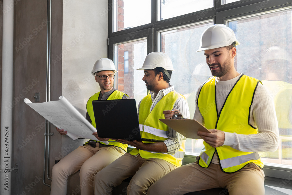 architecture, construction business and people concept - male architects in helmets with laptop, blueprint and clipboard working at office architecture, construction business and people concept - male architects in helmets with laptop, blueprint and clipboard working at office