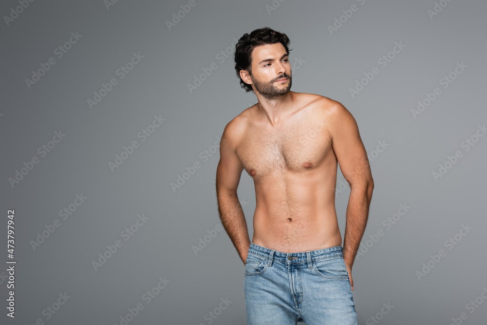 good-looking and muscular man in jeans looking awat isolated on grey