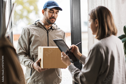 shipping, mail service and people concept - delivery man with parcel box and customer signing digital form in tablet pc computer at home