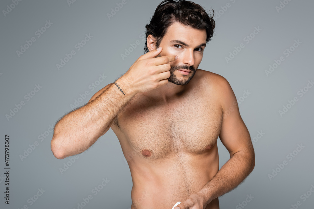 Fototapeta premium tattooed and shirtless man applying cosmetic cream on face isolated on grey