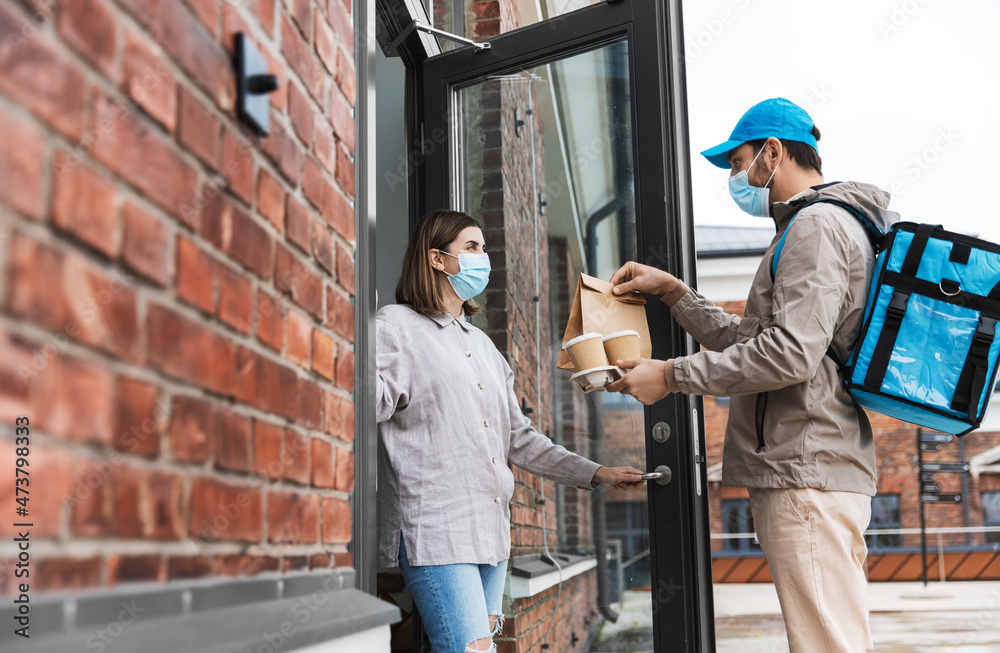 food shipping, pandemic and people concept - delivery man in mask with thermal insulated bag giving order and coffee to female customer at home food shipping, pandemic and people concept - delivery man in mask with thermal insulated bag giving order and coffee to female customer at home