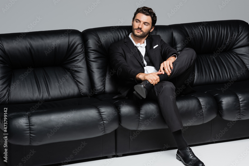 bearded man in formal wear sitting on black sofa on grey bearded man in formal wear sitting on black sofa on grey
