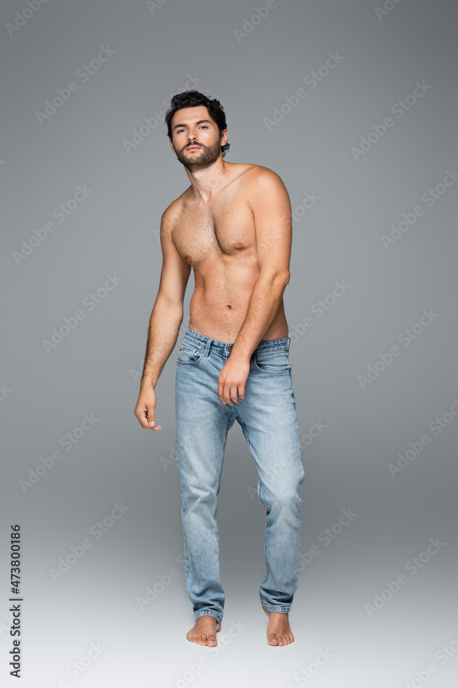 full length of good-looking and muscular man in jeans looking at camera on grey full length of good-looking and muscular man in jeans looking at camera on grey