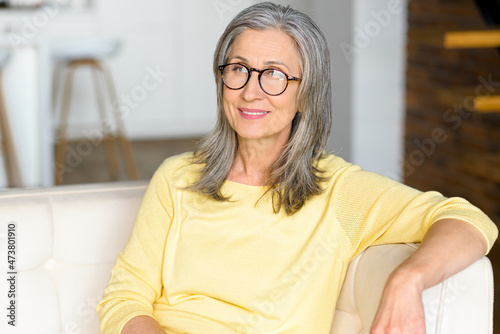 Close-up portrait of contemporary senior woman wearing stylish eyewear looks at the camera and smiles, an elderly female resting at home, spending calm weekend