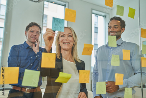 Smiling businesswoman writing on adhesive note while discussing with male colleagues in board room