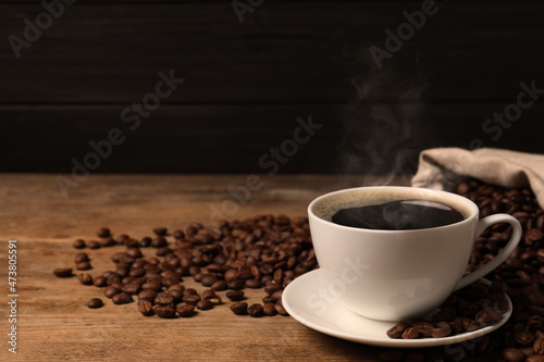 Cup of aromatic hot coffee and beans on wooden table. Space for text