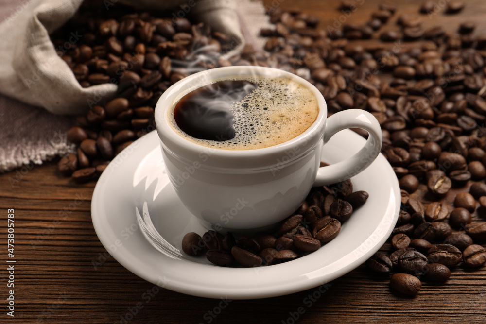 Cup of aromatic hot coffee and beans on wooden table Cup of aromatic hot coffee and beans on wooden table