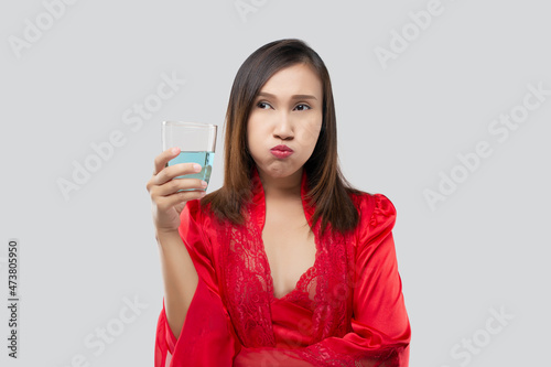 Fotografie Woman in silk nightwear wearing red robes rinsing your mouth with mouthwash after brushing after waking up to start your mornings