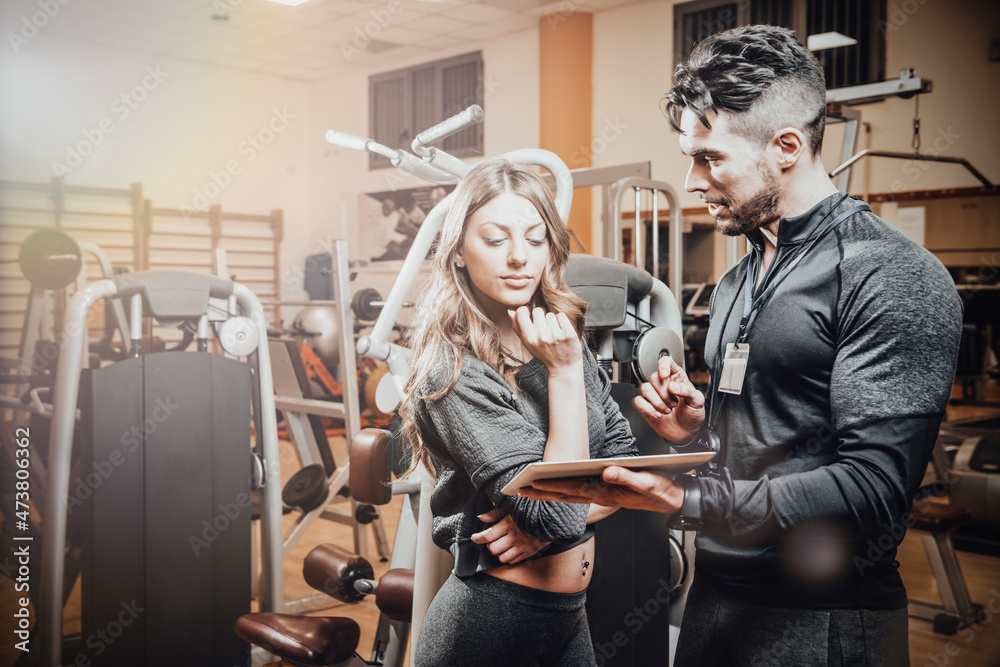 Man and woman looking at each other in gym. Athletic man holding digital tablet and looking at woman.