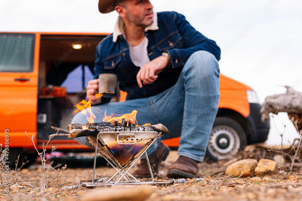 Man crouching near wood burning stove while looking away during camping Man crouching near wood burning stove while looking away during camping