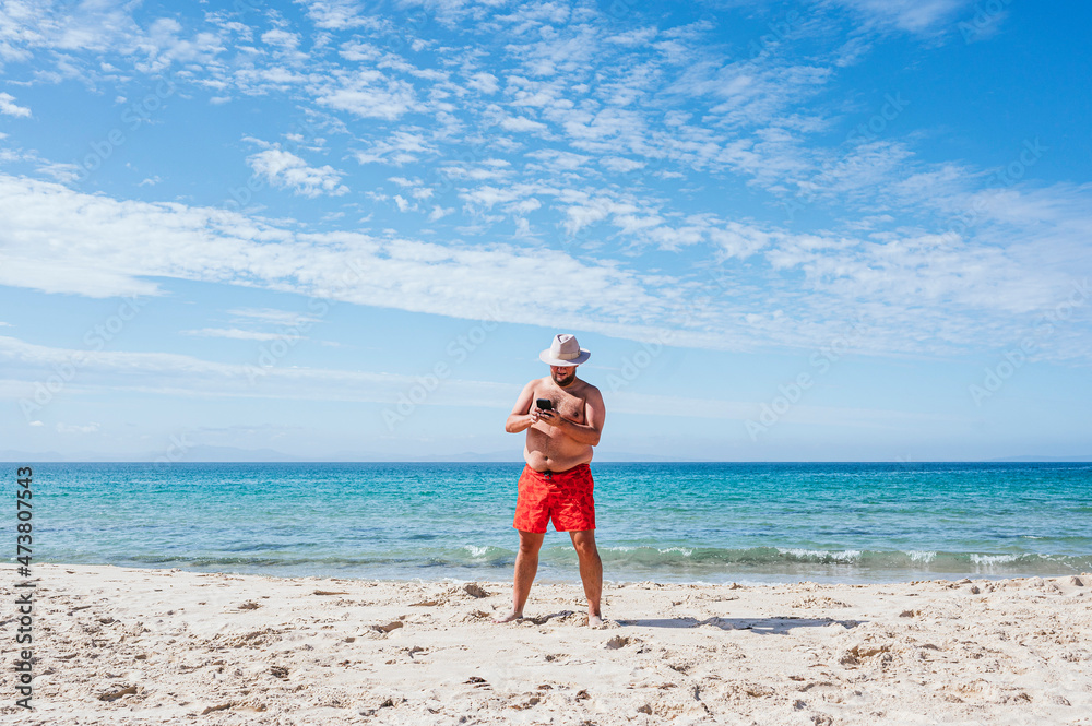 Shirtless gay man using mobile phone at beach during vacation Shirtless gay man using mobile phone at beach during vacation