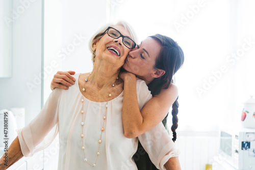 Mid adult woman with arm around kissing grandmother cheek at home photo