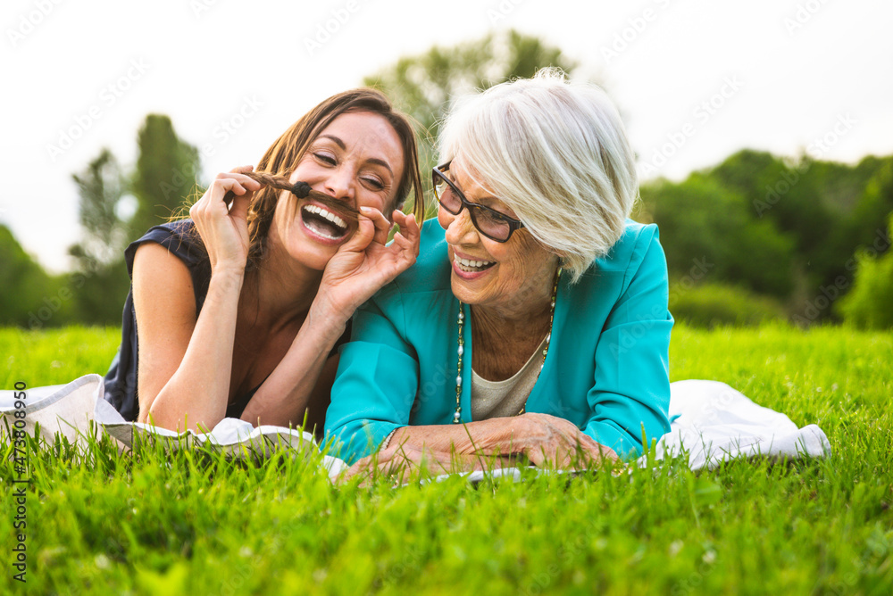 Cheerful granddaughter playing with hair while lying by grandmother on meadow Cheerful granddaughter playing with hair while lying by grandmother on meadow
