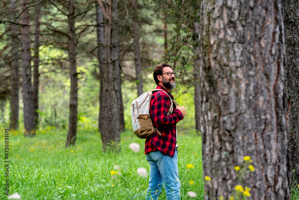 Smiling mature man with backpack walking in green forest Smiling mature man with backpack walking in green forest
