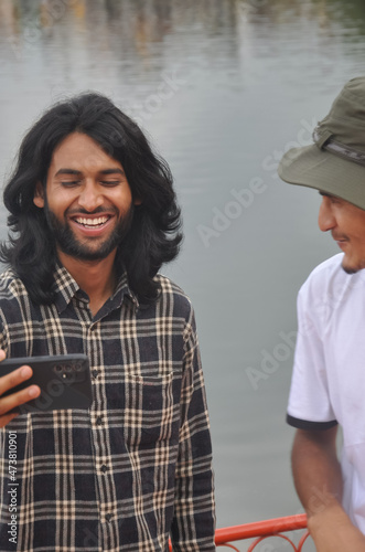 Two male friends having fun while taking selfie together in beside of lake