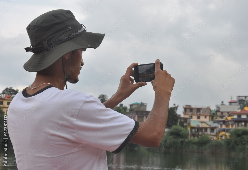 Obraz premium Back view of a male tourist taking photo of landscape with smartphone during cloudy weather